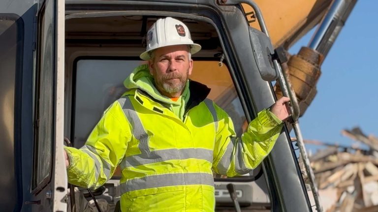 Kevin wearing hardhat standing on his excavator at construction site.