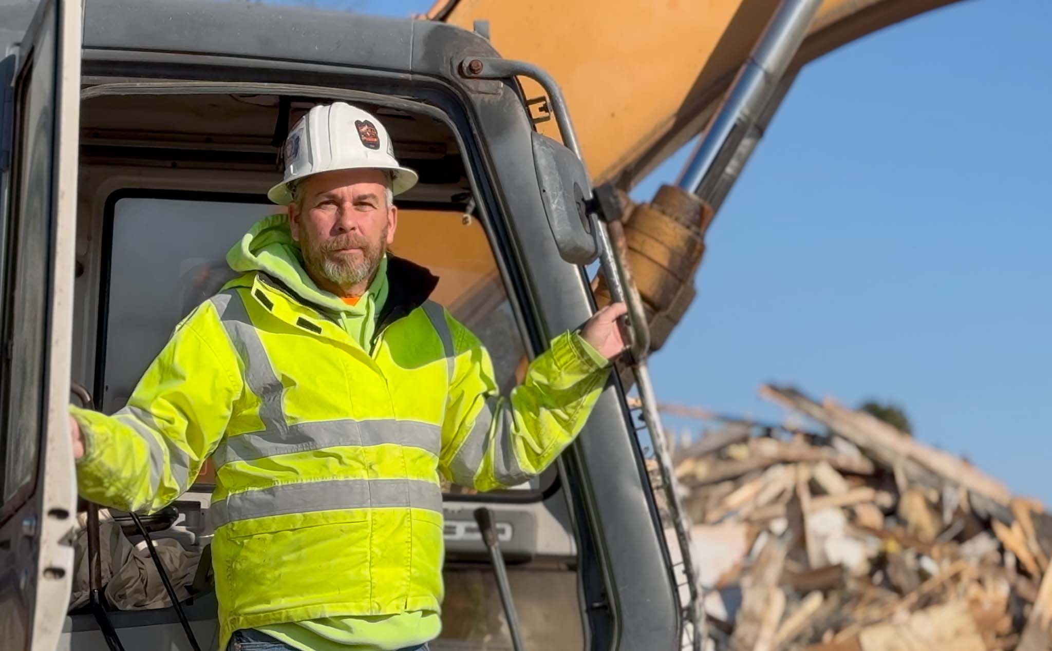 Kevin wearing hardhat standing on his excavator at construction site.