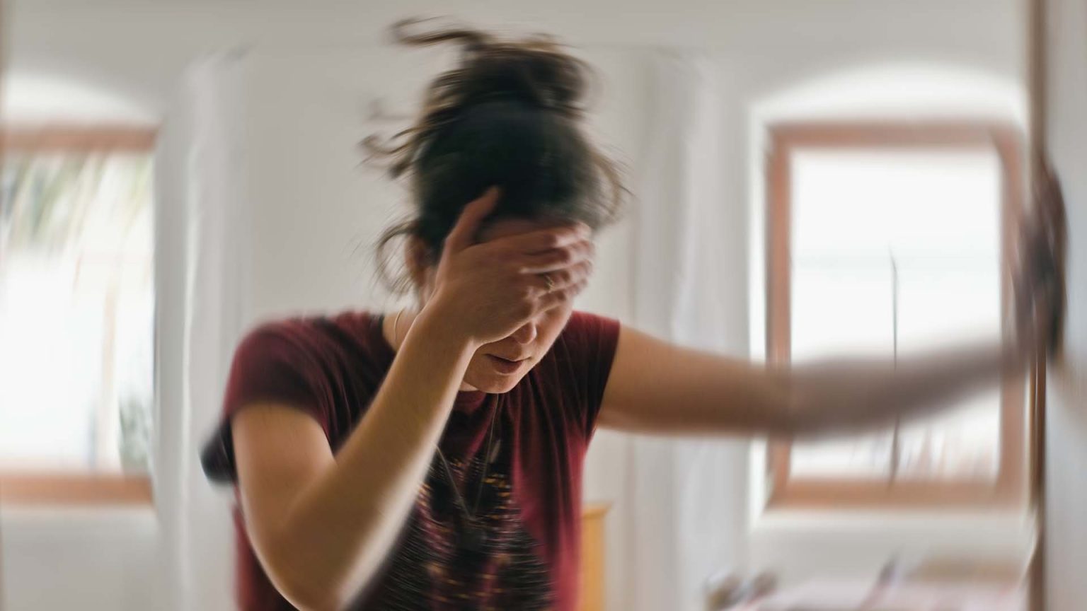 Blurred photo of woman suffering from dizziness holding head and wall.