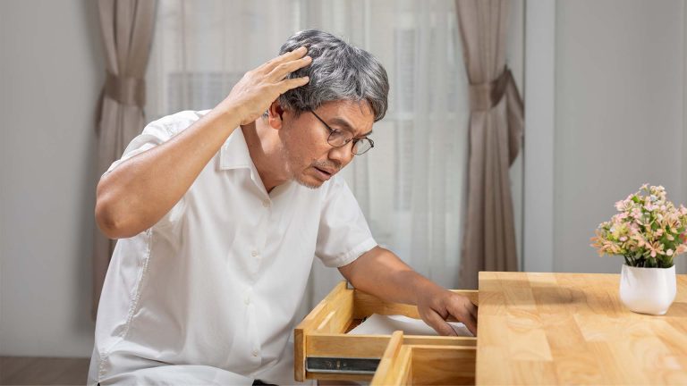 Asian man searching drawers for forgotten items.